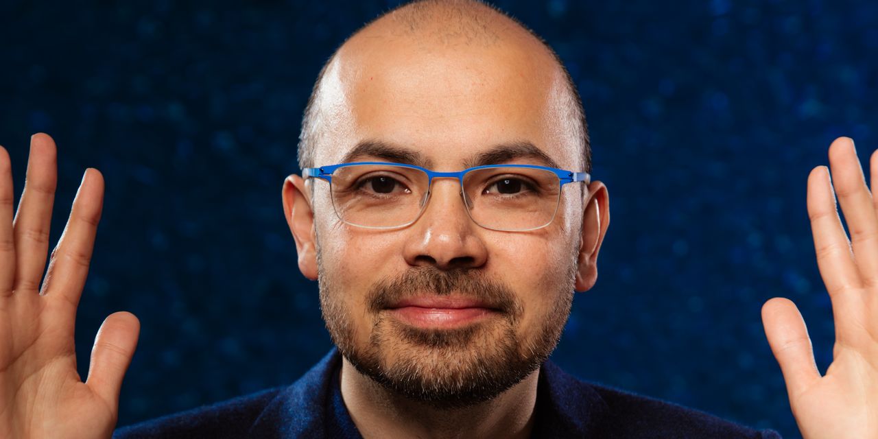 Headshot of Demis Hassabis in front of a plain blue background